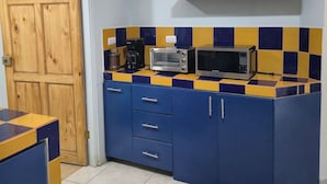 Eine Küche mit Holztür, blauen Schränken, einer Mikrowelle, einem Toaster und einem Regal mit einer Pflanze.