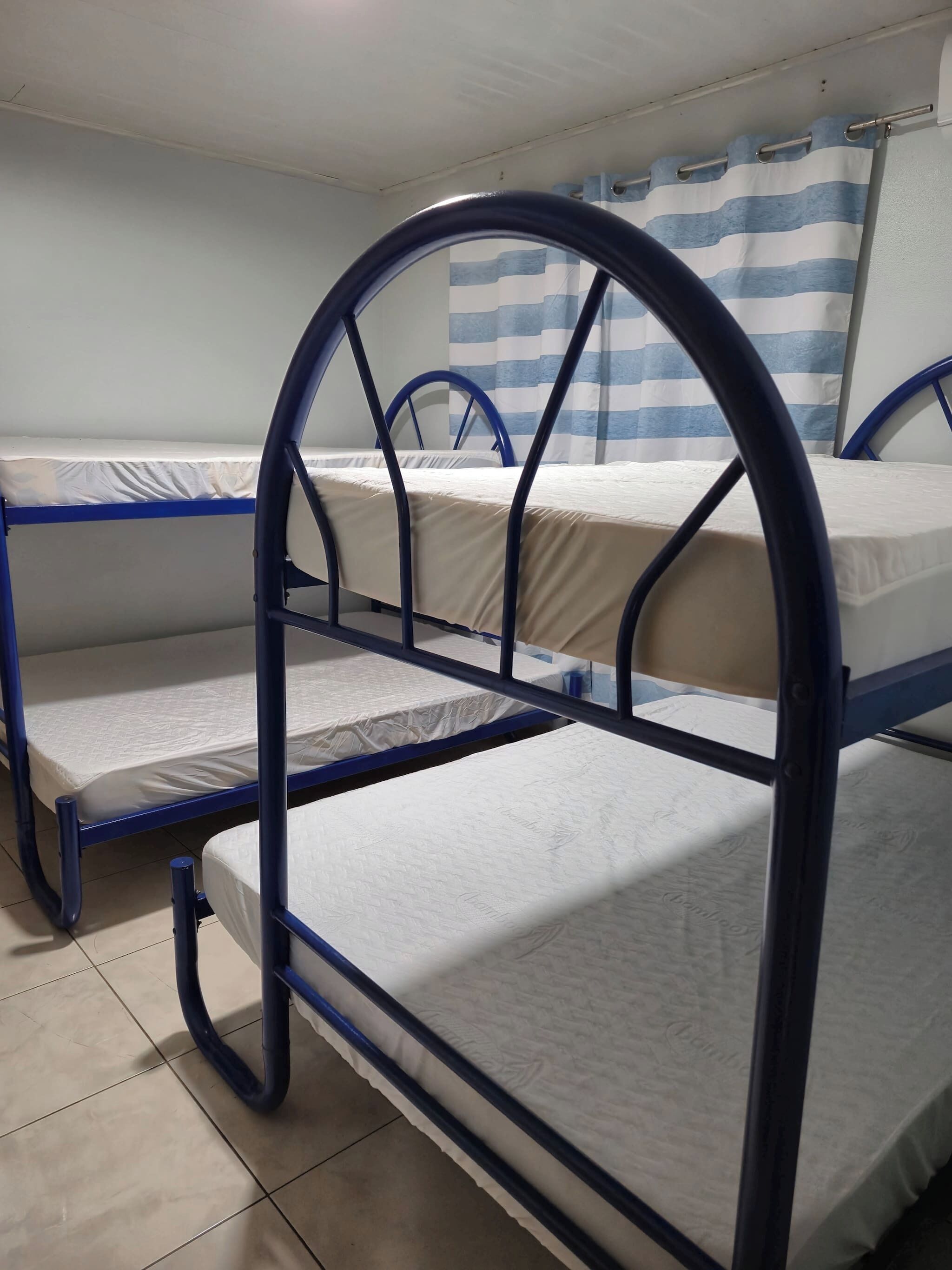 A bunk bed room with a striped curtain, tiled floor, and metal railings.