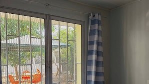 Ein Zimmer mit einem Bett, einem Fenster mit Insektengitter und Blick auf Gartenmöbel.