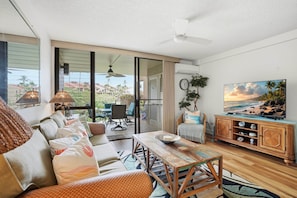 A spacious living room with a sofa, coffee table, and a TV mounted on the wall. - Maui Bliss Garden Lanai, Dual AC, Beach, Pool, Gym (Kihei)