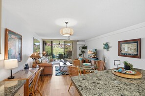A modern living room with a dining area, large windows, and a ceiling fan. - Maui Bliss Garden Lanai, Dual AC, Beach, Pool, Gym (Kihei)