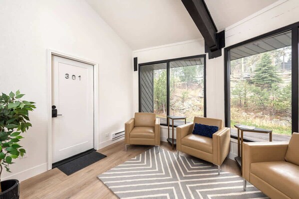 A modern room with a door marked '301', two leather chairs, a small table, and a large window offering a view of trees.