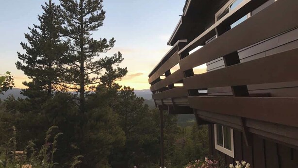 Een modern gebouw met een schuin dak en grote ramen, omringd door bomen en een tuin.