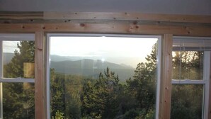 Een kamer met een groot raam dat uitzicht biedt op een bebost landschap en bergen.