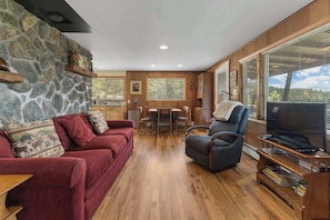 A cozy living room with a stone wall, a red sofa, a blue armchair, a wooden coffee table, and a television.