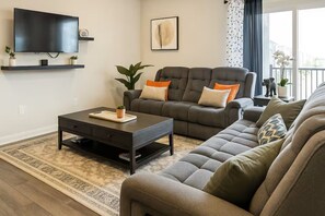 Ein Wohnzimmer mit Sofa, Couchtisch, Fernseher und einem großen Fenster.