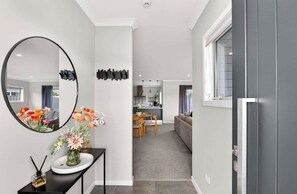 Ein modernes Interieur mit einem runden Spiegel, einem Konsolentisch mit Blumen, einem Essbereich mit einer Couch und einer Küche im Hintergrund.
