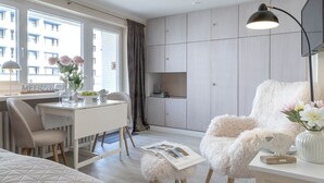 Ein modernes Zimmer mit Essbereich, einem gemütlichen Sessel, einem weißen Schreibtisch und einem Bücherregal.