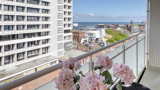 Ein Hochhaus mit Balkonen und Meerblick, ein Blumenarrangement auf einem Balkon.