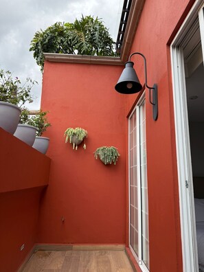 Pared exterior roja con una ventana, una puerta y dos macetas colgantes.