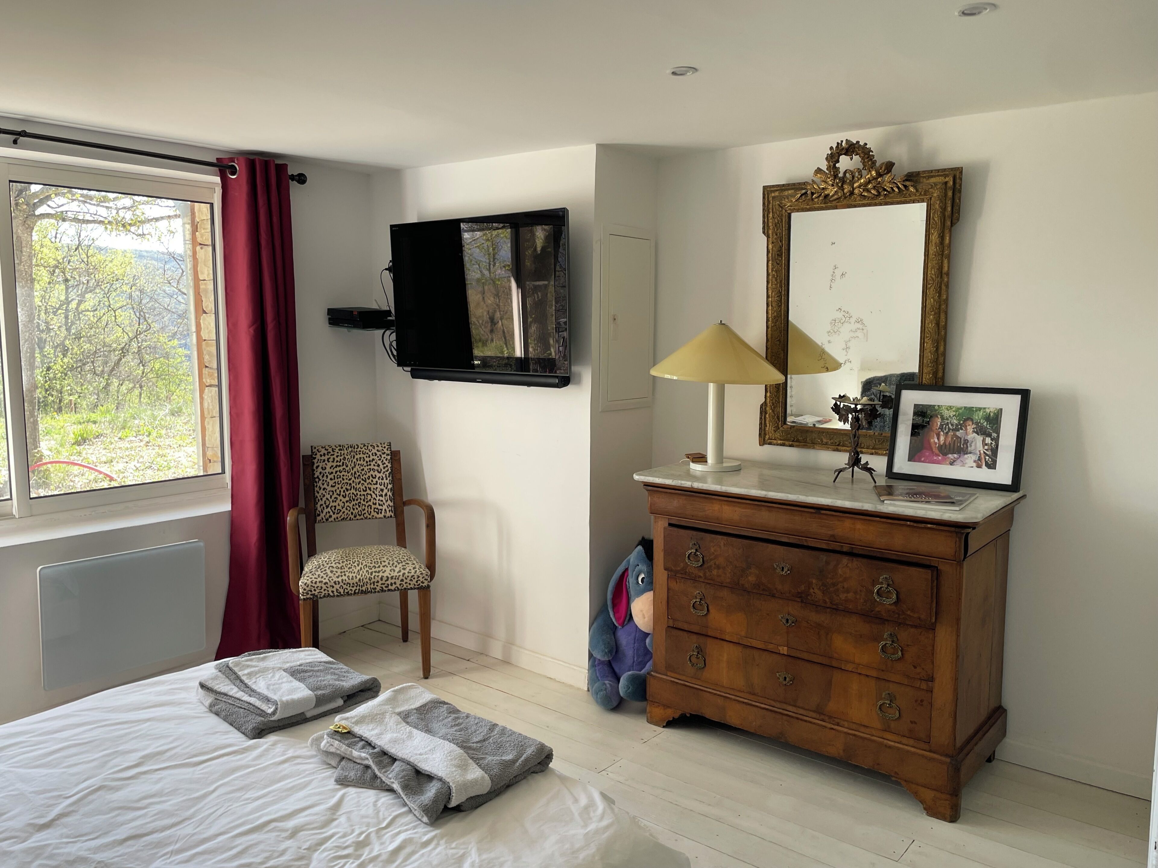 A bedroom with a bed, a chair, a dresser, a mirror, and a window with curtains.
