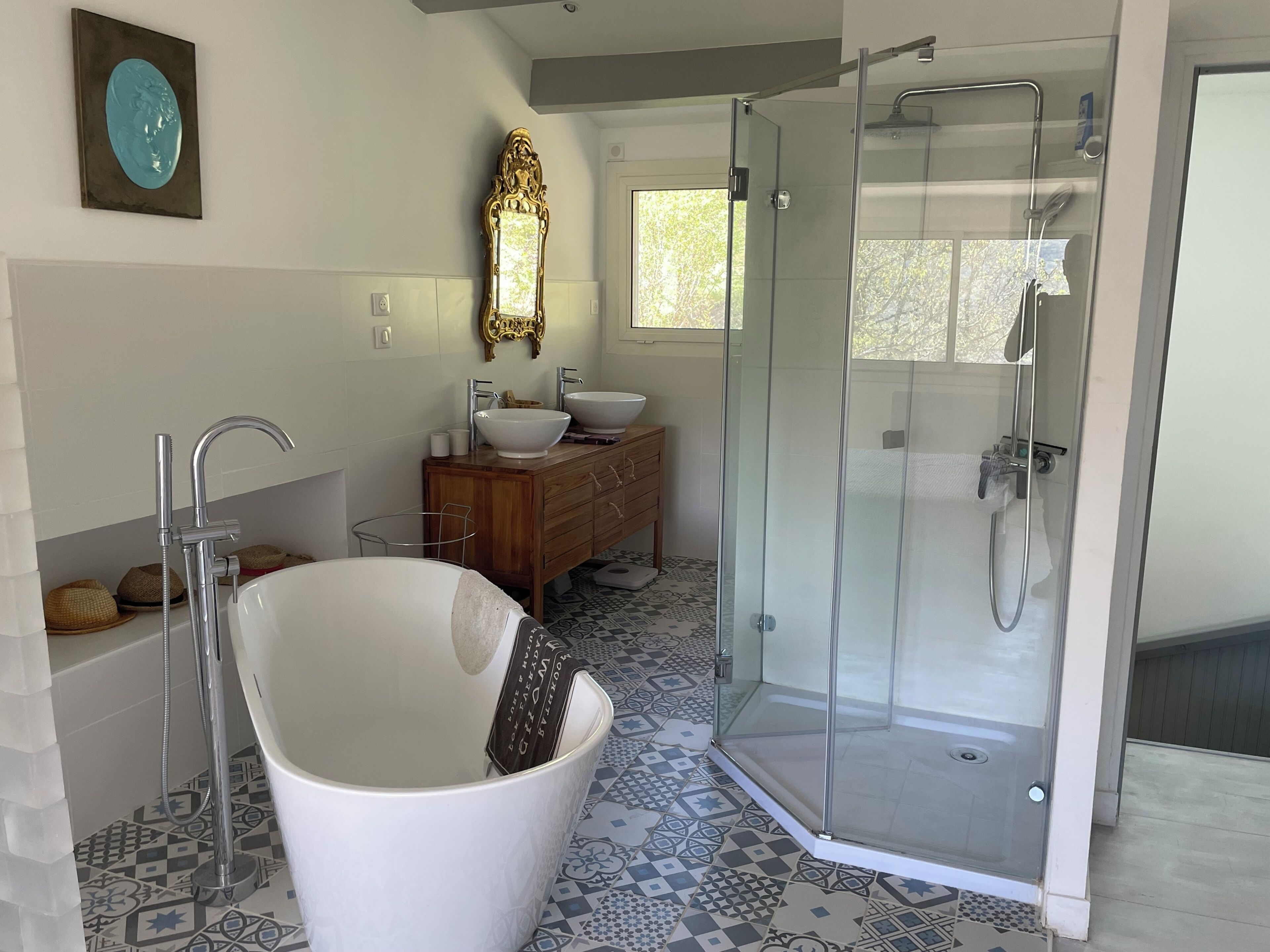 Une salle de bain moderne avec une baignoire sur pieds, une douche à parois de verre, un meuble-lavabo en bois et des carreaux de sol à motifs.