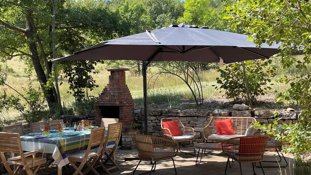 Ulkoterassi, jossa on tiilestä tehty leivinuuni, puinen terassi, rottingista valmistetut huonekalut ja ruokailuun katettu pöytä.