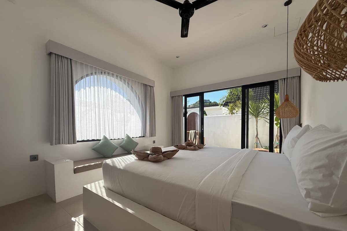 Ein modernes Schlafzimmer mit einem großen Bett, einer Sitzecke und Blick durch die Glastür.