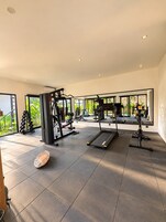 Un gimnasio moderno con equipo de ejercicio, ventanas amplias y vistas a zonas verdes.
