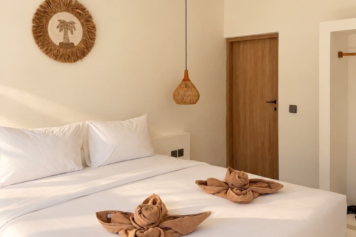 A bedroom with a bed, a ceiling fan, a wall-mounted light, and a door.