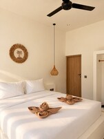 A bedroom with a bed, a ceiling fan, a wall-mounted light, and a door.