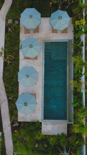 A rectangular swimming pool with four light blue umbrellas and wooden lounge chairs.