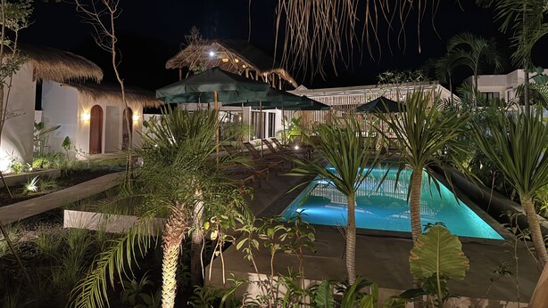 A pool area with lounge chairs, a thatched-roof structure, and tropical plants. - Kairos boutique sports hotel (Selong Belanak)