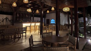 An indoor dining area with thatched roof ceilings, wicker furniture, and hanging light fixtures. - Kairos boutique sports hotel (Selong Belanak)