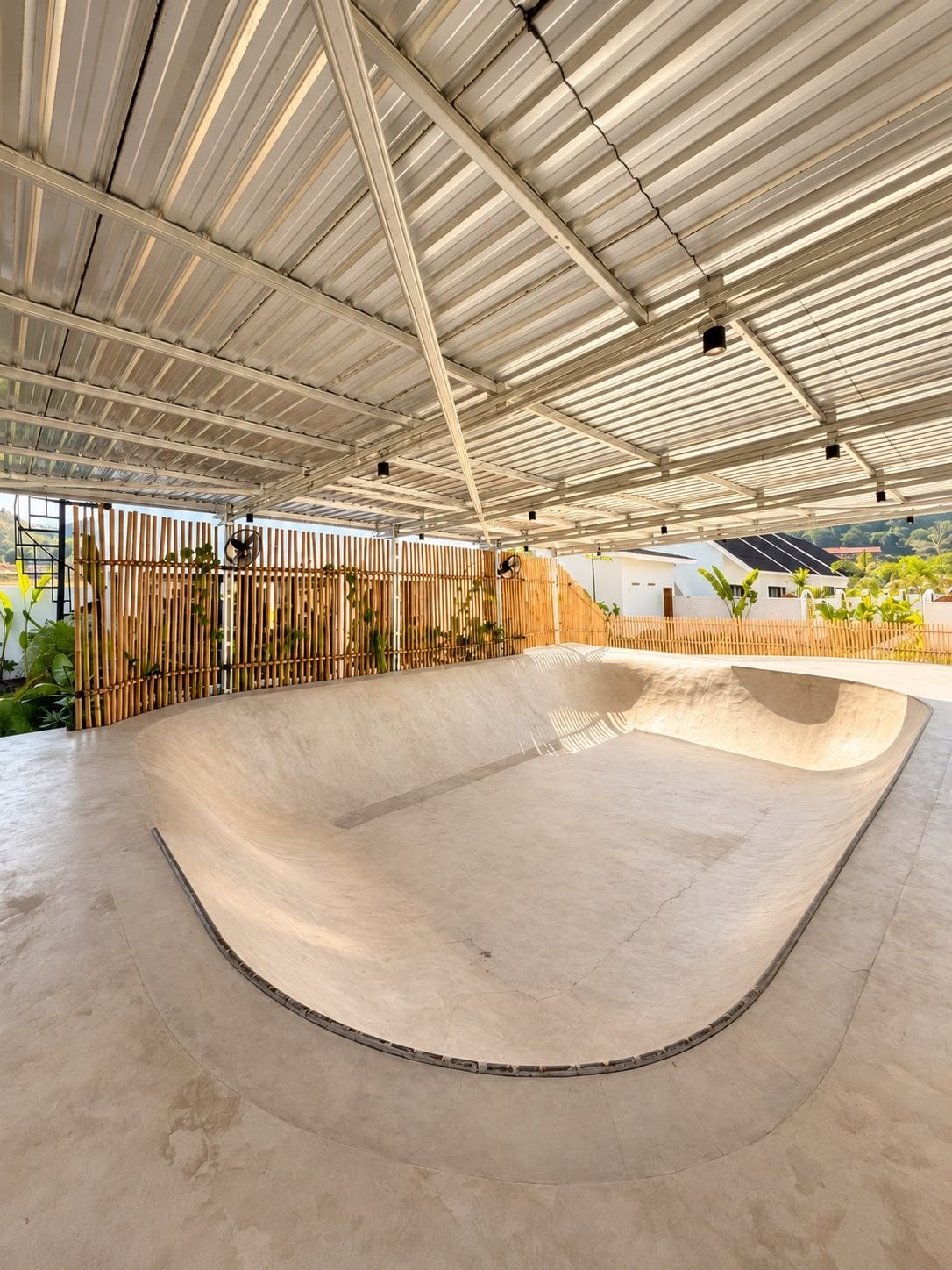 A skate park with a concrete bowl, metal roof, and bamboo fencing.