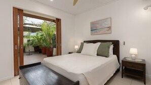 Un dormitorio con cama, mesitas de noche, un cuadro y vistas a través de un ventanal abierto.