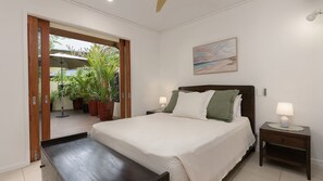 A bedroom with a bed, bedside tables, a painting, and a view through an open door. - Surya 11 | Port Douglas (PORT DOUGLAS)