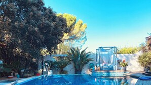 Piscina com deck revestido, rodeada por árvores e uma pérgula com cobertura.