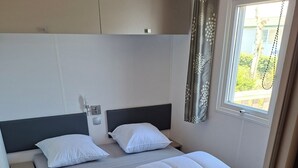 Ein Schlafzimmer mit zwei Betten, einem Fenster mit Vorhängen und einem kleinen Nachttisch.