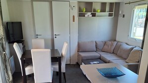 Ein kompakter Wohnbereich mit Küchenzeile, einer Couch, einem Esstisch mit Stühlen und einem Fernseher.