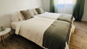 Un letto matrimoniale con copriletto bianco e verde, un comodino e una finestra con tende verdi.