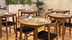 Zona pranzo con tavoli e sedie in legno, una lampada decorativa a sospensione e piante in vaso.