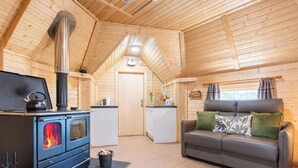 Interior acolhedor de uma cabana com lareira a lenha, um sofá e uma cozinha compacta.