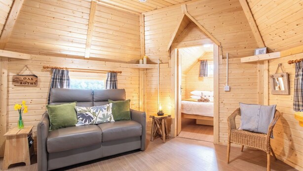 Interior acolhedor de uma cabana com um sofá, uma cadeira de vime, uma cama e uma mesinha.