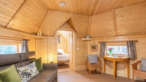 Interior acolhedor de uma cabana de madeira, com sofá, cadeiras, mesa de jantar e uma cama.