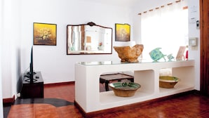 Een receptiegedeelte met een bureau met glazen blad, een spiegel, ingelijste kunstwerken aan de muur en een houten deur.