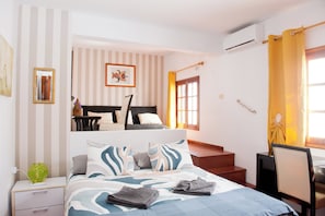 Ein Hotelzimmer mit einem Bett, einem Schreibtisch, einem Sessel, einem Fenster mit Vorhängen, einer Treppe und einer wandmontierten Klimaanlage.