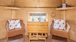 Interior acolhedor de uma cabana com duas cadeiras de vime, uma mesa de madeira e uma janela com vista.