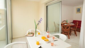 Un balcón con una mesa de comedor dispuesta para dos personas, incluyendo una jarra de jugo de naranja, una botella de vino y un florero con flores.