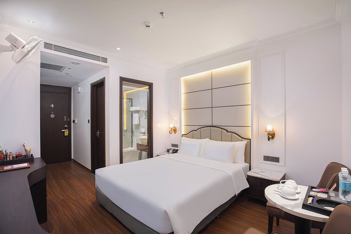 A hotel room with a large bed, bedside tables, a desk, and a bathroom visible through an open door.