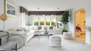 A modern living room with a white sofa, glass coffee table, and a view of greenery outside. - Luxury & Private 6BR Single House • Summer Retreat w/ Parking & Pet-Friendly 35 (Randolph)
