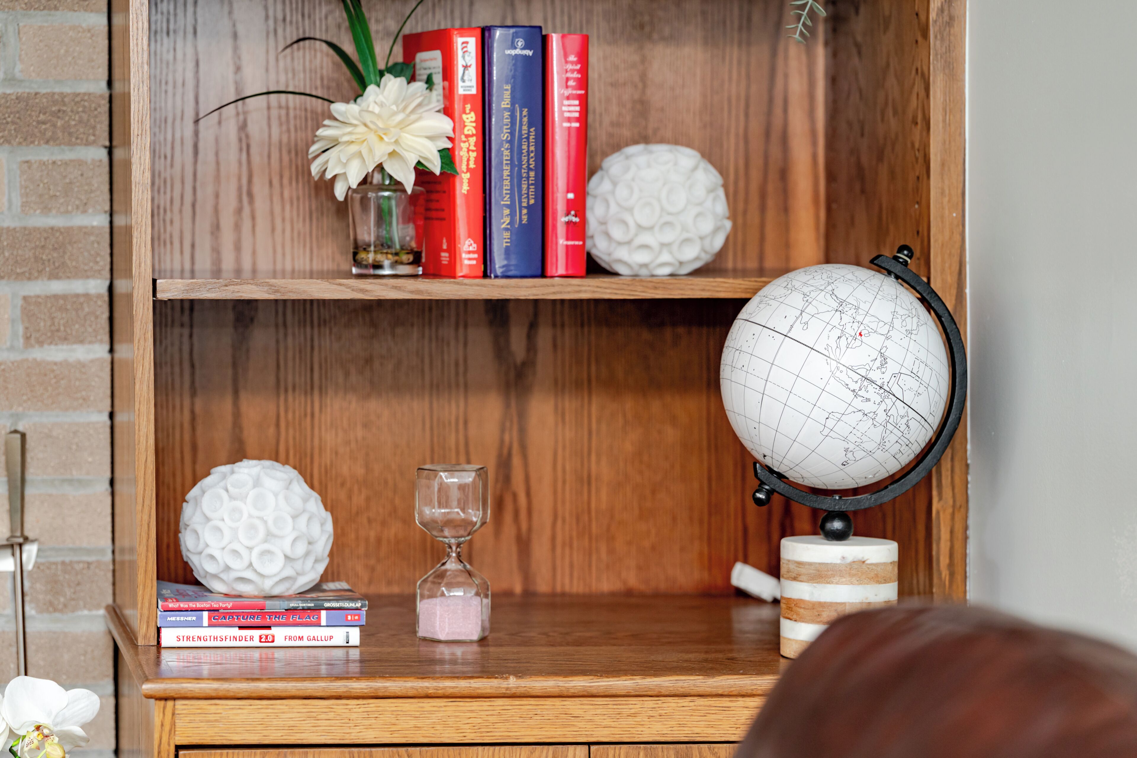 A wooden bookshelf with books, a globe, decorative spheres, and an hourglass.