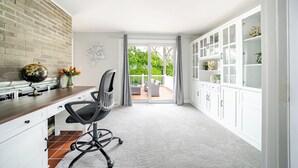 A modern interior with a brick wall, a desk with a globe, a chair, a balcony with a view of greenery, and white cabinetry. - Luxury & Private 6BR Single House • Summer Retreat w/ Parking & Pet-Friendly 35 (Randolph)