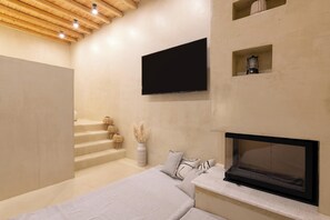 A modern bedroom with a TV, fireplace, and a staircase. - Antheia Traditional House in Archaggelos (Rhodes)