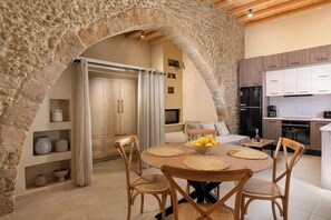 A stone archway leading to a dining area with a round table, chairs, and a kitchen in the background. - Antheia Traditional House in Archaggelos (Rhodes)