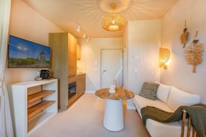 Ein modernes Wohnzimmer mit einem weißen Sofa, einem runden Couchtisch, einem an einer Holzablage montierten Fernseher und einer Küche im Hintergrund.