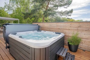Ein Whirlpool auf einer Holzdielen-Terrasse mit einem Blumentopf in der Nähe.