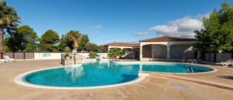 Une piscine à bords incurvés, un espace détente couvert et un terrain clôturé.