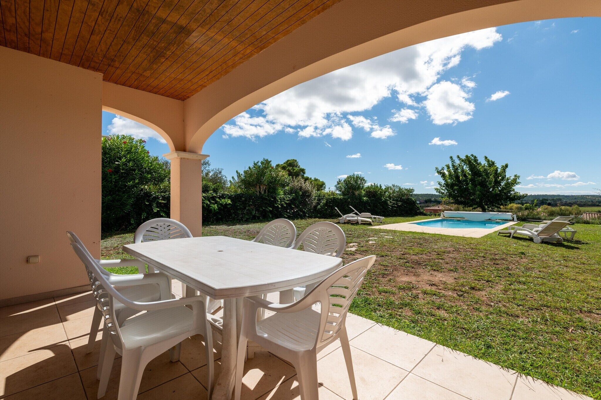 An outdoor patio with a table and chairs, a swimming pool, and a view of the surrounding landscape.