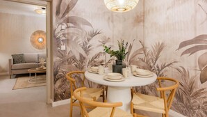A dining area with a round table, four chairs, a vase with greenery, and a wall with a tropical leaf pattern. - Bali Blizz apartment 18 with sauna, whirlpool and terrace in Benz (Benz)